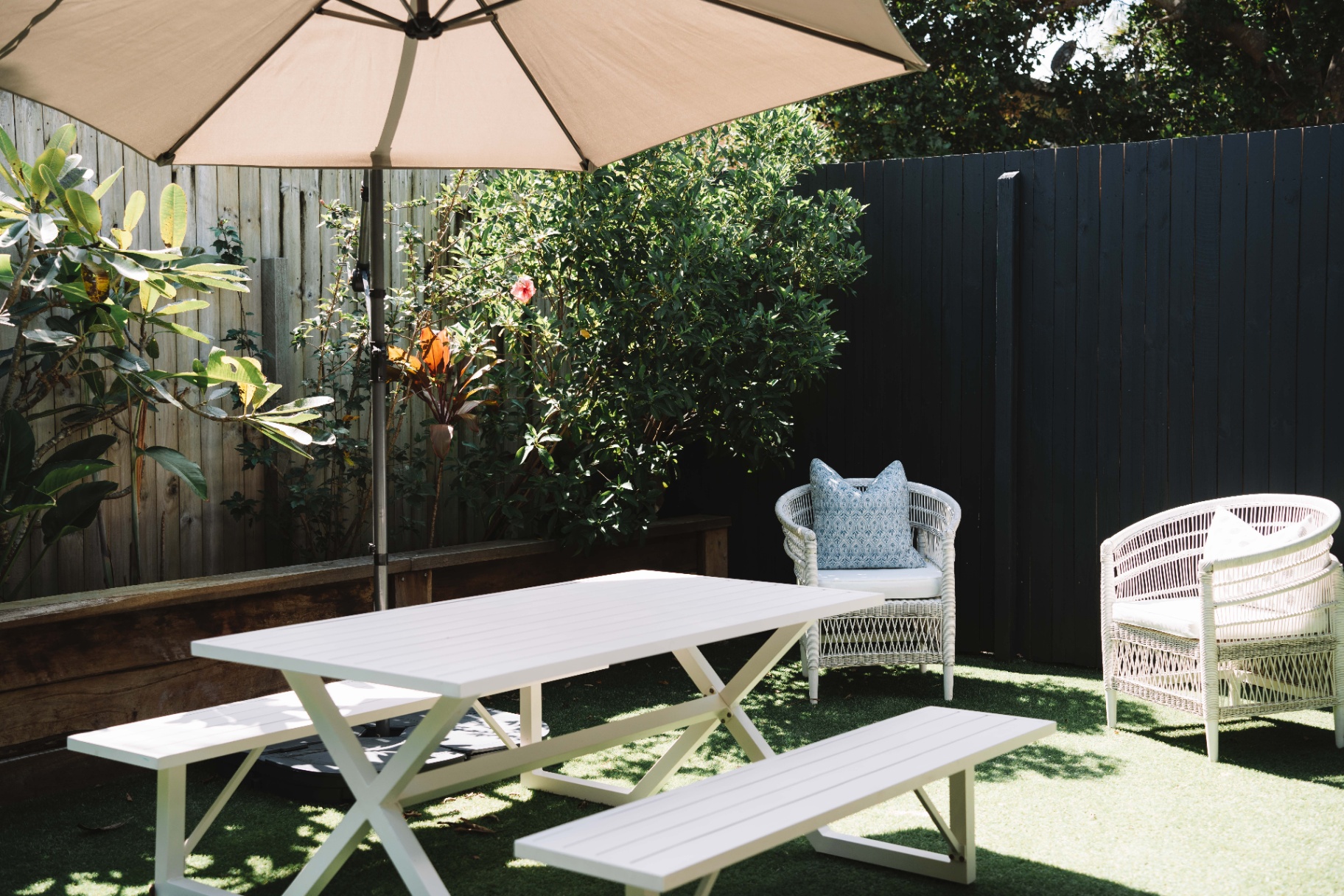 Private outdoor courtyard at Hjemme Noosa with white picnic table, umbrella and garden seating.