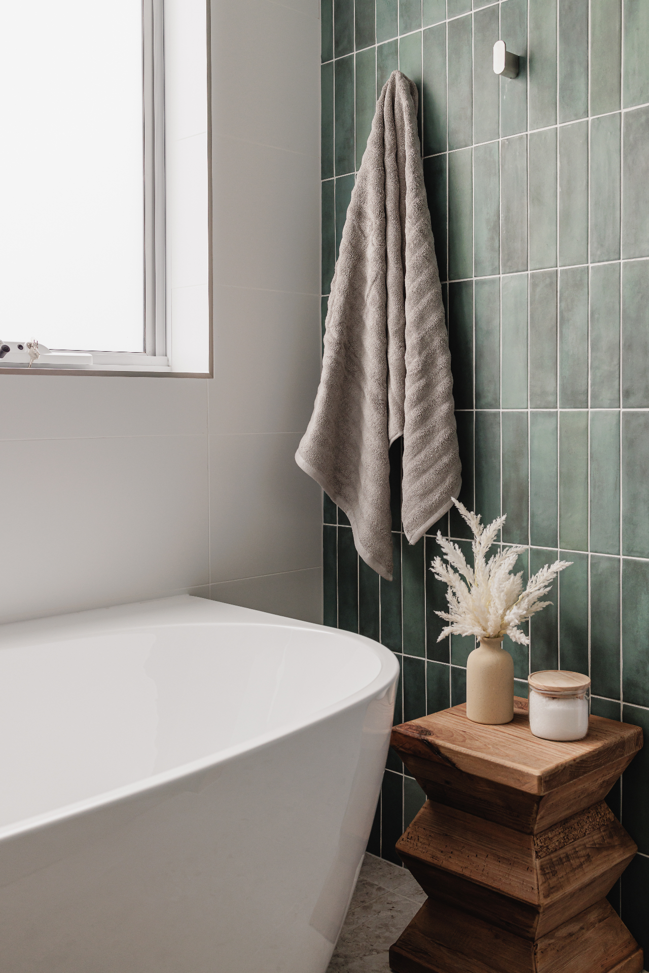 Bathroom detail photo with bathtub, towel, green tiles and timber stool at Hjemme Hobart